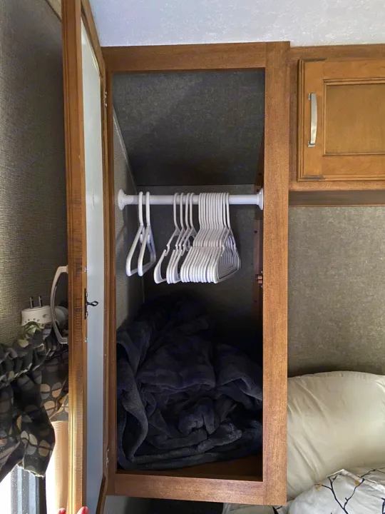 Open closet in an RV rental bedroom, showing white hangers on a rod and a dark blanket below. Efficient RV storage.. Keystone RV Springdale 2017