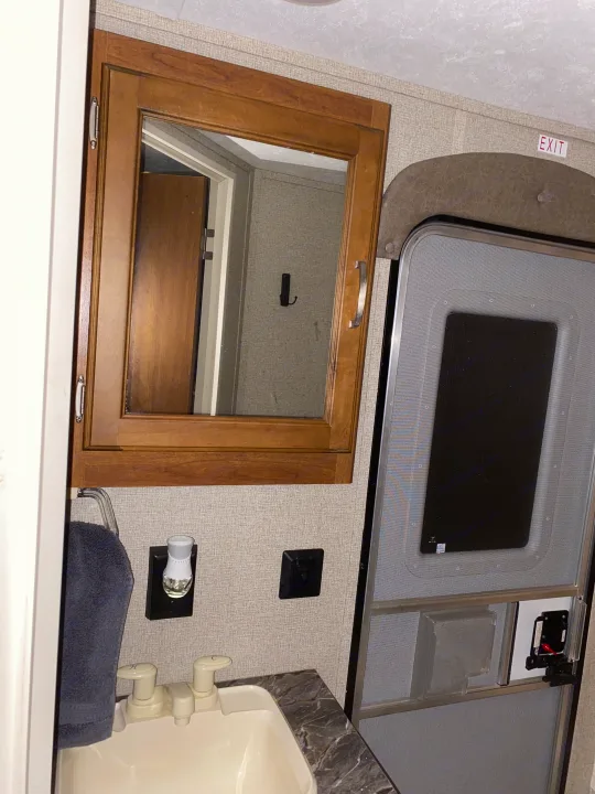 Inside an RV rental: Compact bathroom sink, mirror cabinet, and screen exit door with an 'EXIT' sign.. Keystone RV Springdale 2017