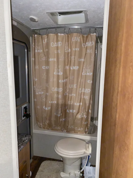 RV rental bathroom with a toilet and shower, featuring a "Love Camp Live" curtain—perfect for your next camping adventure.. Keystone RV Springdale 2017