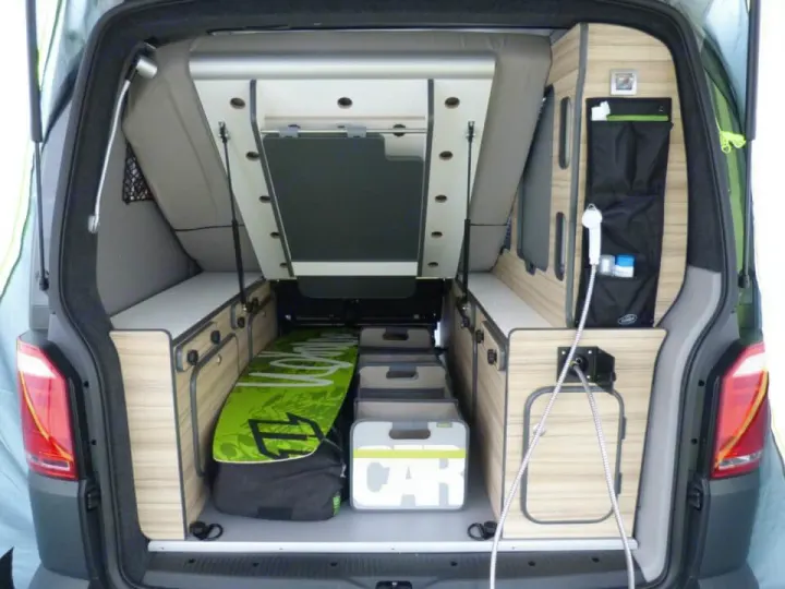 This RV rental interior showcases a compact camper van with a bed, smart storage, and outdoor shower setup.. Volkswagen Transporter T6.1 2022