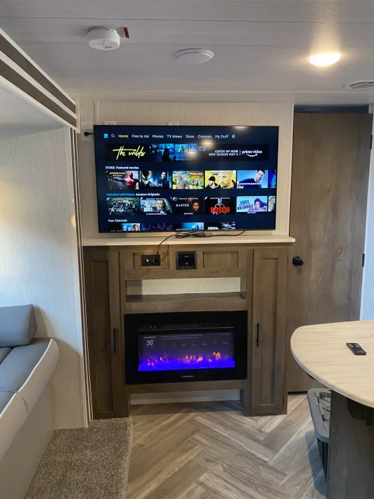 Cozy RV rental interior with a large TV displaying streaming content, an electric fireplace, and comfortable seating. Perfect for mobile living.. Forest River 263BHXL 2022