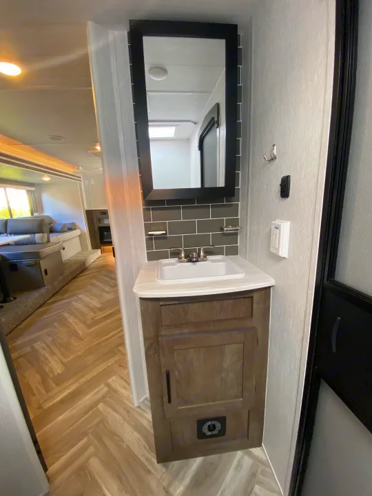 Modern RV rental interior: compact bathroom with sink & mirror, leading to a spacious living area with lounge.. Forest River 263BHXL 2022