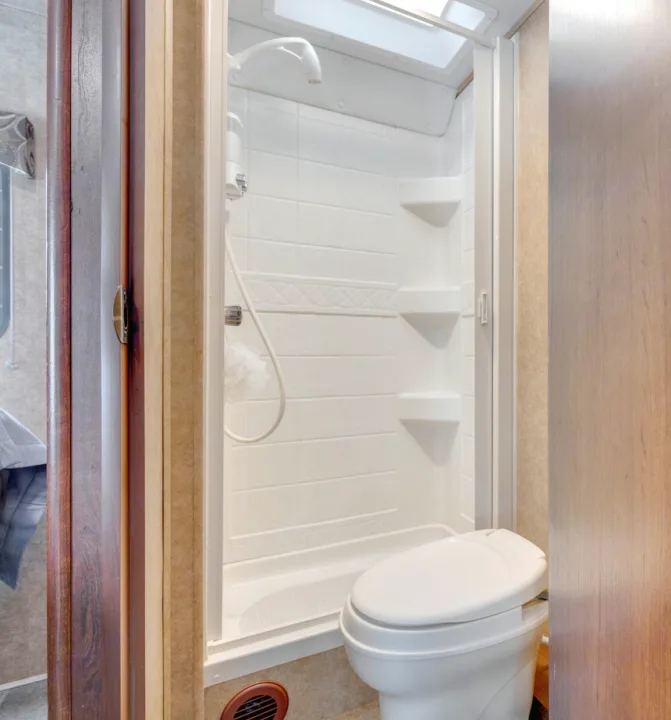 Step into this clean RV rental bathroom, showcasing a practical white shower stall with shelves and an adjacent toilet.. Forest River Sunseeker 2014