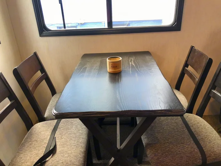 RV rental dinette set: a dark wood table with four upholstered chairs, seen by a window. A candle is on the table.. Forest River Cherokee Alpha Wolf 2022