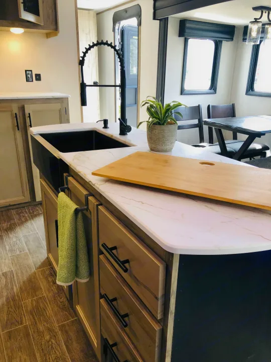 Modern RV rental kitchen: sleek black farmhouse sink, white countertops, kitchen island & dining area.. Forest River Cherokee Alpha Wolf 2022