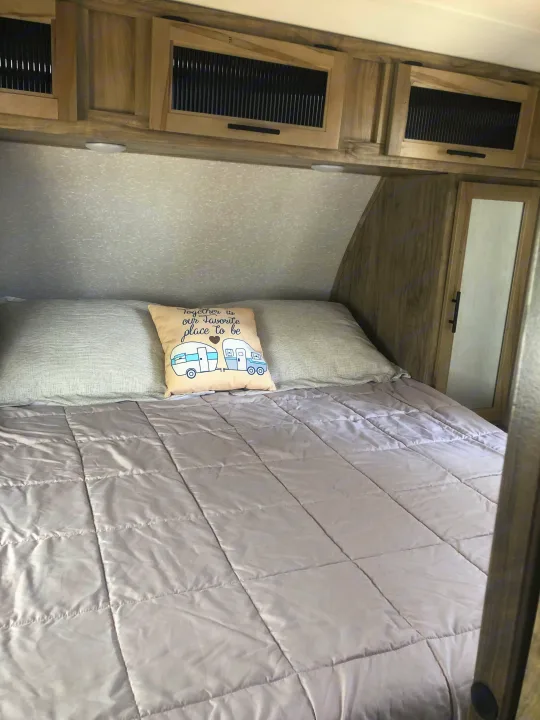 Relax in this cozy RV rental bedroom. Features a comfy bed, camper pillow, and slatted overhead storage cabinets.. Forest River Cherokee Alpha Wolf 2022
