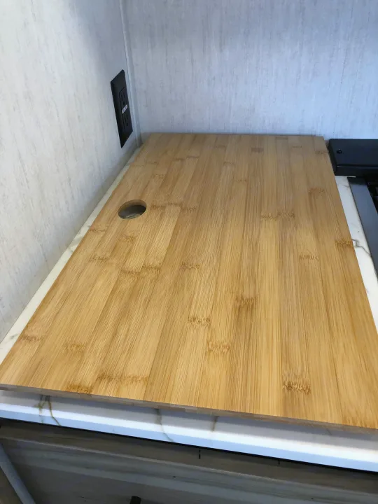 RV rental kitchen counter featuring a large bamboo cutting board with a round hole, next to a wall outlet.. Forest River Cherokee Alpha Wolf 2022
