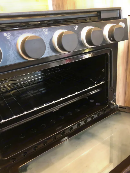 An open oven inside an RV rental, showing two wire racks and the control panel with knobs.. Forest River Cherokee Alpha Wolf 2022