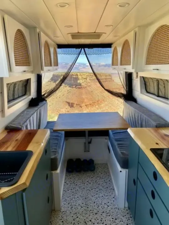 Inside a stylish rv rental, showing a cozy camper van interior with bench seating, kitchen, and panoramic canyon views.. Freightliner Sprinter 2011