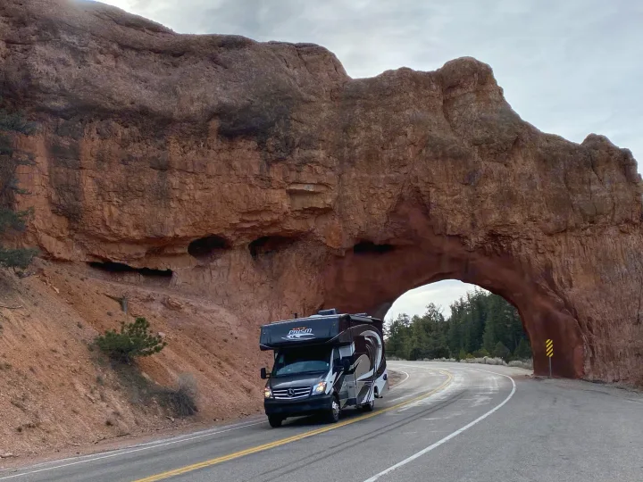 An RV rental drives through the stunning Red Canyon natural arch on a scenic Utah road trip.. Coachmen Prism 2019