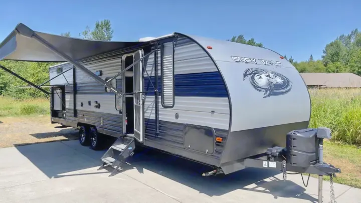 Grey Wolf RV rental: A modern, grey travel trailer with an extended awning and open door, parked on concrete on a sunny day.. Forest River Cherokee Grey Wolf 2020