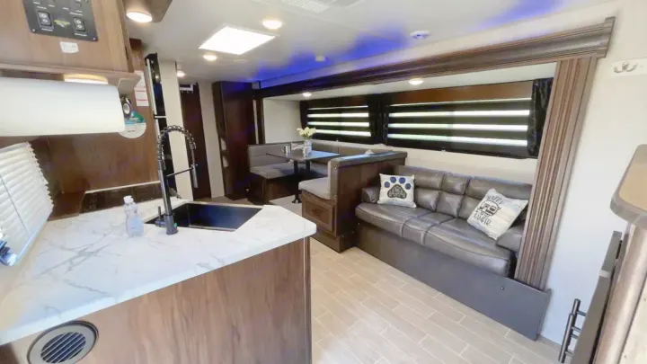 This bright rv rental interior features a modern kitchen, dining booth, and sofa with throw pillows under accent lighting.. Forest River Cherokee Grey Wolf 2020