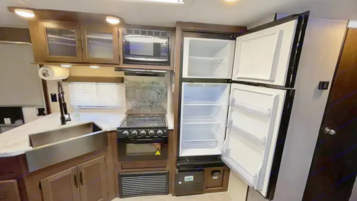 This rv rental features a well-equipped kitchen with an open refrigerator, microwave, stove, and a stylish sink.. Forest River Cherokee Grey Wolf 2020