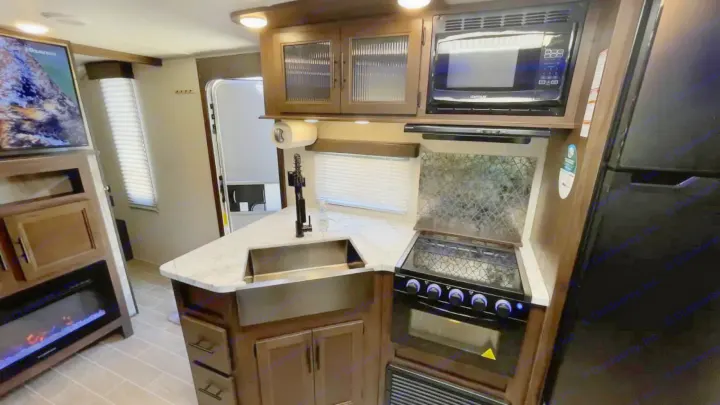 Spacious rv rental kitchen featuring microwave, stove, sink, & fridge. Living area has a TV, fireplace, and modern decor.. Forest River Cherokee Grey Wolf 2020