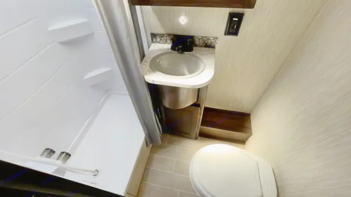 Inside an RV rental: a compact bathroom featuring a white shower, marble-top sink, and white toilet on tiled floor.. Forest River Cherokee Grey Wolf 2020