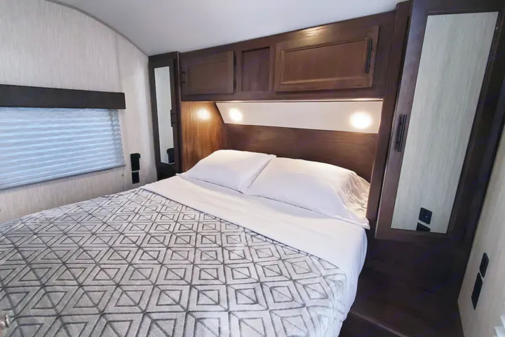 Cozy rv rental bedroom features a comfortable bed, overhead cabinets, reading lights, window blind, and mirrored closet.. Forest River Cherokee Grey Wolf 2020