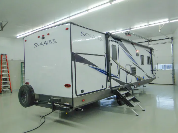White Solaire travel trailer, a spacious RV rental option, parked indoors with extended steps.. Forest River Palomino Solaire 2021