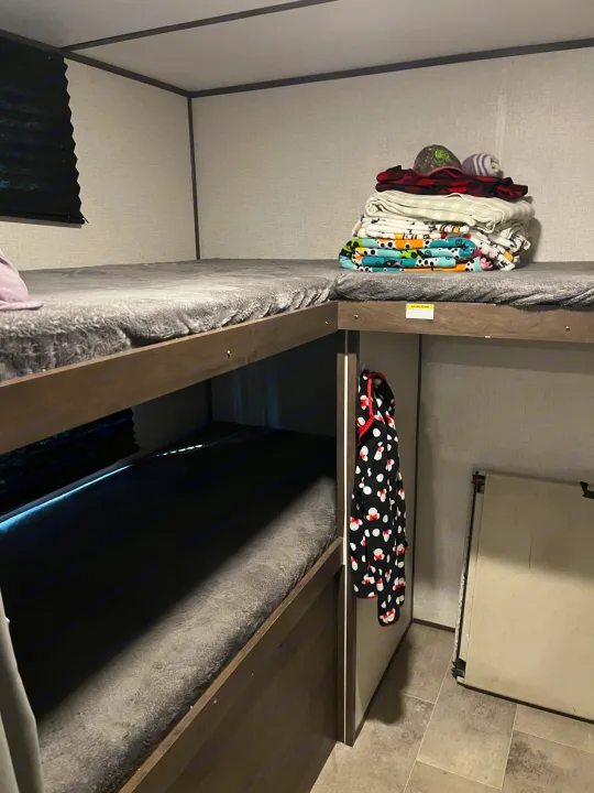 RV rental bunk beds: a cozy interior sleeping area with stacked blankets and a hanging robe.. Coleman QBWE295 2021