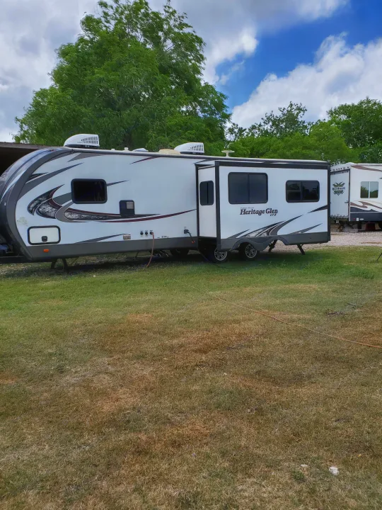 White "Heritage Glen" RV rental parked on a grassy lot, featuring an extended slide-out, under a partly cloudy sky.. Forest River Wildwood 2019