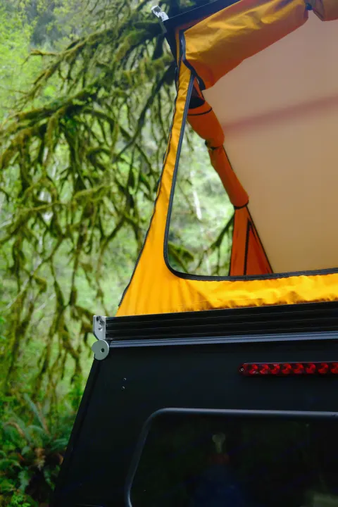 RV rental pop-up tent setup in a lush, mossy forest. Features bright orange fabric and a black camper shell, perfect for adventures.. Toyota Tacoma 2018