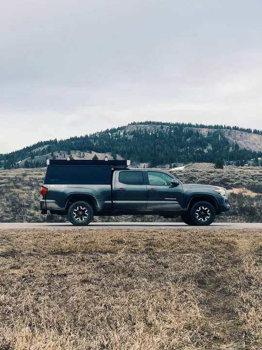 A dark grey Toyota Tacoma pickup with a truck camper, offering a compact rv rental option for exploring rugged terrain.. Toyota Tacoma 2018