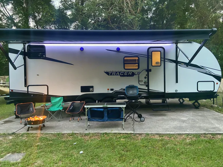 Cozy RV rental campsite with illuminated awning, fire pit, grill, and chairs for outdoor relaxation.. Other Tracer 2022