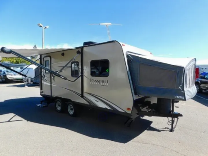 Tan Passport hybrid travel trailer rv rental with an extended awning on a sunny lot.. Keystone RV Passport Express 2016