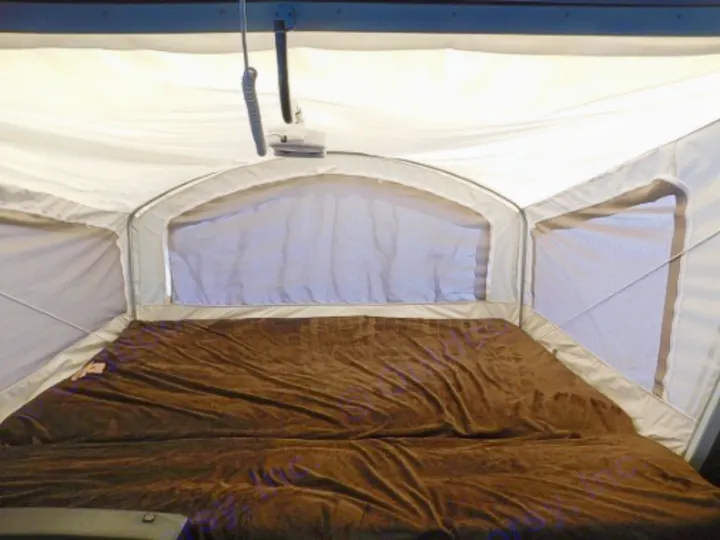 Inside an RV rental: a spacious pop-up camper bed with brown blanket & screened windows. Perfect for camping!. Keystone RV Passport Express 2016