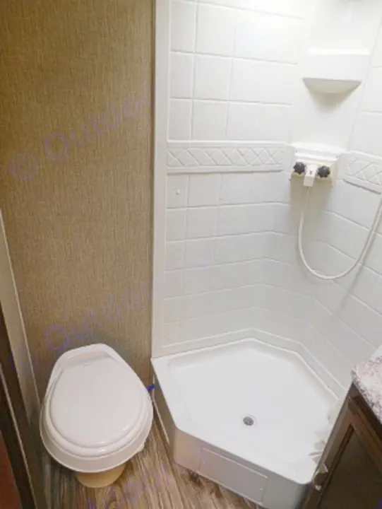 Inside an RV rental bathroom: a white, compact toilet sits next to a corner shower with controls. Functional space for travel.. Keystone RV Passport Express 2016