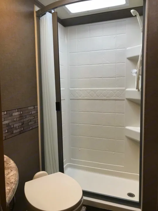 This RV rental's compact bathroom includes a bright white shower with a clear curved door, toilet, and partial sink view.. Thor Chateau 2019