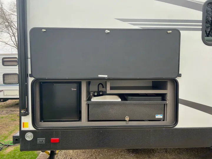 This RV rental features an outdoor kitchen with a Midea mini-fridge, sink with faucet, and pull-out cooktop.. Other Other 2021