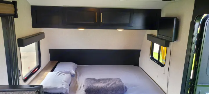 Explore this RV rental bedroom interior with a comfy bed, black overhead cabinets, and two windows. Ready for travel.. Forest River Cherokee Wolf Pup 2022