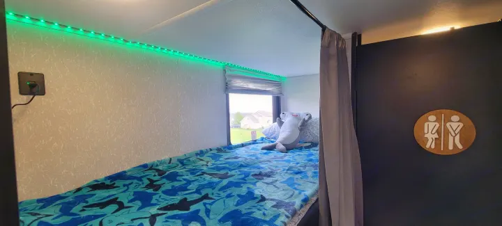 Inside a comfy RV rental bunk, featuring shark bedding, green LED lights, and a fun bathroom door sign.. Forest River Cherokee Wolf Pup 2022