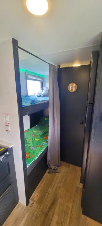 Inside an RV rental: cozy bunk beds with dinosaur blankets, a bathroom door with a restroom sign, and a compact interior.. Forest River Cherokee Wolf Pup 2022