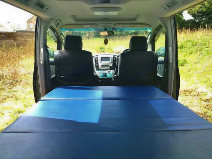 This RV rental shows a minivan interior with a blue, flat sleeping platform stretching to the front seats, ready for camping.. Toyota Other 2022