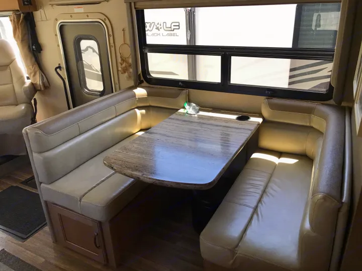 RV rental interior featuring a cozy U-shaped dinette with light-colored seating and a faux-marble table.. Thor Motor Coach A.C.E 2018