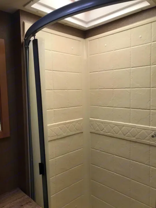 Inside a modern RV rental shower: off-white textured walls, a dark curved rod, and bright ceiling light.. Thor Motor Coach A.C.E 2018