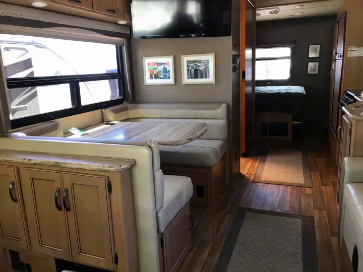 Spacious RV rental interior: dining booth, wall-mounted TV, kitchen, and a glimpse into the cozy bedroom.. Thor Motor Coach A.C.E 2018