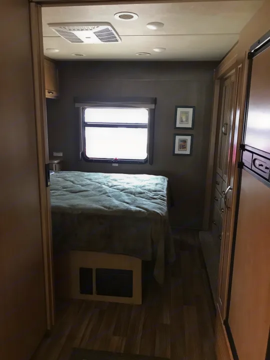 Cozy RV rental bedroom seen from doorway, with a comfortable bed, window, ceiling AC, and built-in storage.. Thor Motor Coach A.C.E 2018
