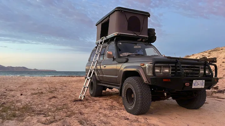 Overland-ready Toyota Land Cruiser with rooftop tent on a beach, ideal for an RV rental alternative for off-grid camping adventures.. Toyota LandCruiser HJ61 VX 1989