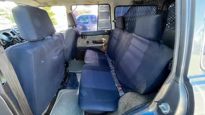 View of the rear seats inside an RV rental, featuring dark fabric upholstery and a protective cargo net.. Toyota LandCruiser HJ61 VX 1989