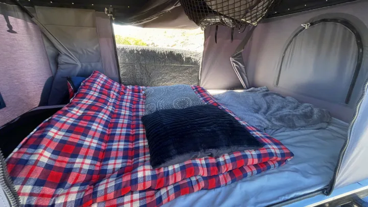 Cozy RV rental interior: a bed with red plaid bedding, gray and black pillows, and a plush gray blanket awaits adventure.. Toyota LandCruiser HJ61 VX 1989
