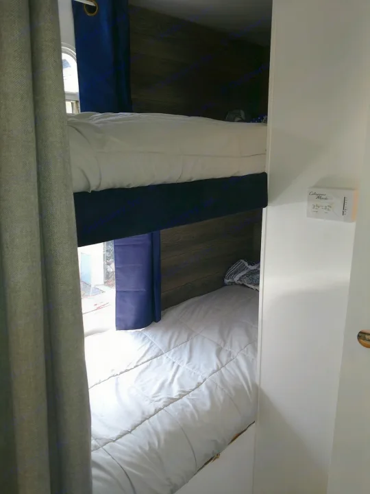 Bunk beds inside an RV rental, featuring white bedding, blue privacy curtains, and a window. Compact sleeping area.. Jayco Jay Flight 2006