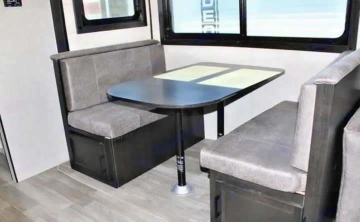 Inside an RV rental: a compact dinette with comfortable grey upholstered bench seating, a dark table, and windows for natural light.. Jayco JayFlight 267BHSW 2022