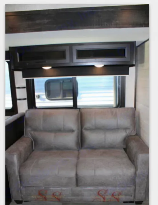 An RV rental interior featuring a comfortable grey sofa, overhead cabinets with lights, and two large windows.. Jayco JayFlight 267BHSW 2022