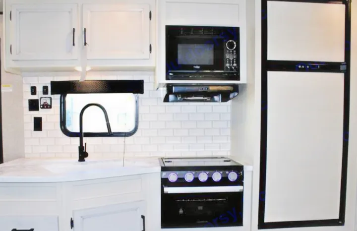 RV rental kitchen: white cabinets, subway tile, black faucet, and modern appliances including stove, microwave, fridge.. Jayco JayFlight 267BHSW 2022
