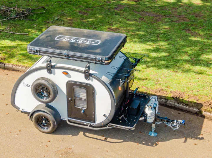 This compact white & black teardrop camper, ideal for rv rental, features a rooftop tent & propane tanks.. Bean Trailer Bean Stock 2022