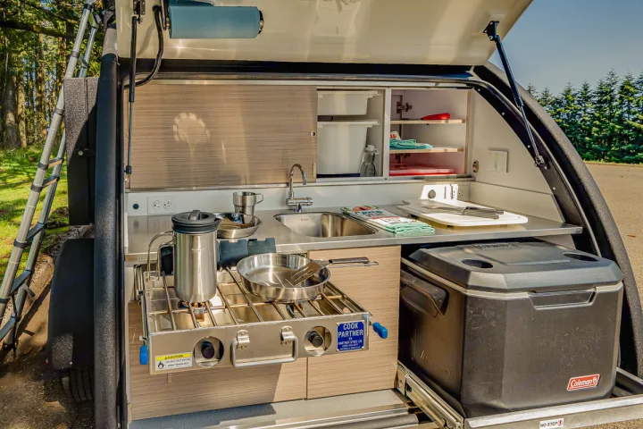 Compact RV rental's rear outdoor kitchen: stove, sink, and Coleman cooler setup for hassle-free camping cooking.. Bean Trailer Bean Stock 2022