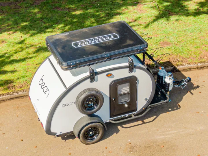 Overhead shot of a compact white Bean teardrop camper, featuring a rooftop tent, ideal for your next RV rental & camping trip.. Bean Trailer Bean Stock 2022