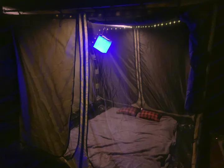 Cozy RV rental sleeping space for camping, featuring a bed, plaid pillows, blue lantern, and string lights.. Toyota 4runner 2003
